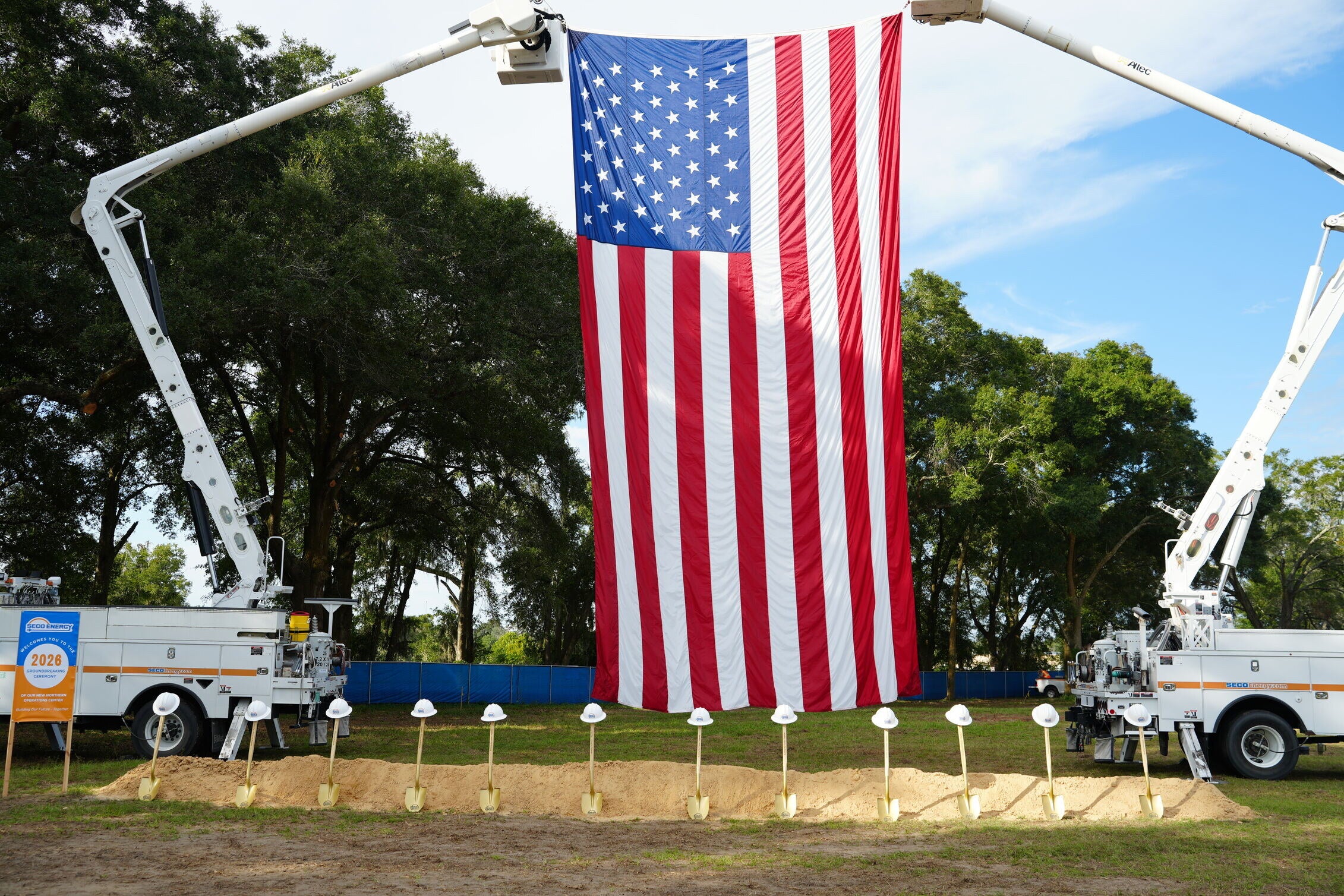SECO Energy’s bucket trucks holding up the United States flag, with shovels and hard hats lined up before the ceremony.